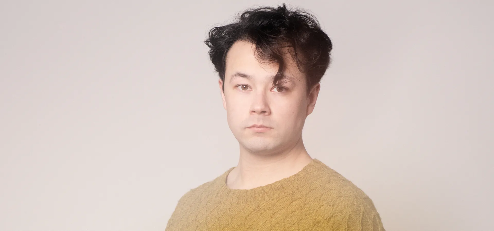 Man met bruin haar staat tegen een muur.